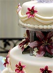 zweistoeckige weisse Hochzeitstorte mit lilafarbenen Lilienblueten